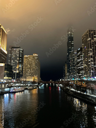 The nocturnal view of the Chicago River illuminates the cityscape with radiant building lights, casting a mesmerizing and vibrant reflection upon the water's surface, painting a captivating and lively
