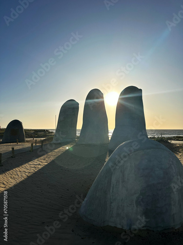 A photo captures La Mano sculpture at Punta del Este, sunlight streaming through the fingers, creating striking shadows and highlighting the iconic artwork's details against the backdrop.