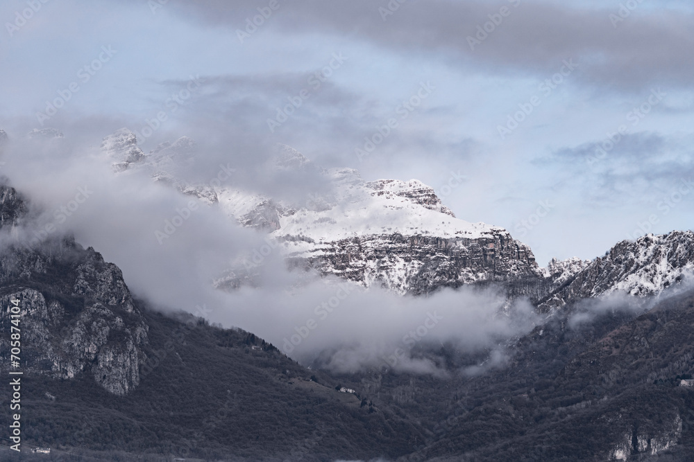 Mountain covered with snow and fog. Alpine landscape in Italy, Europe. Snow-capped mountains against blue sky