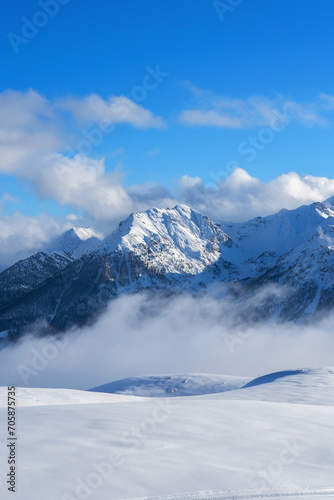 Mountain covered with snow and fog. Alpine landscape in Italy, Europe. Snow-capped mountains against blue sky © photo-lime