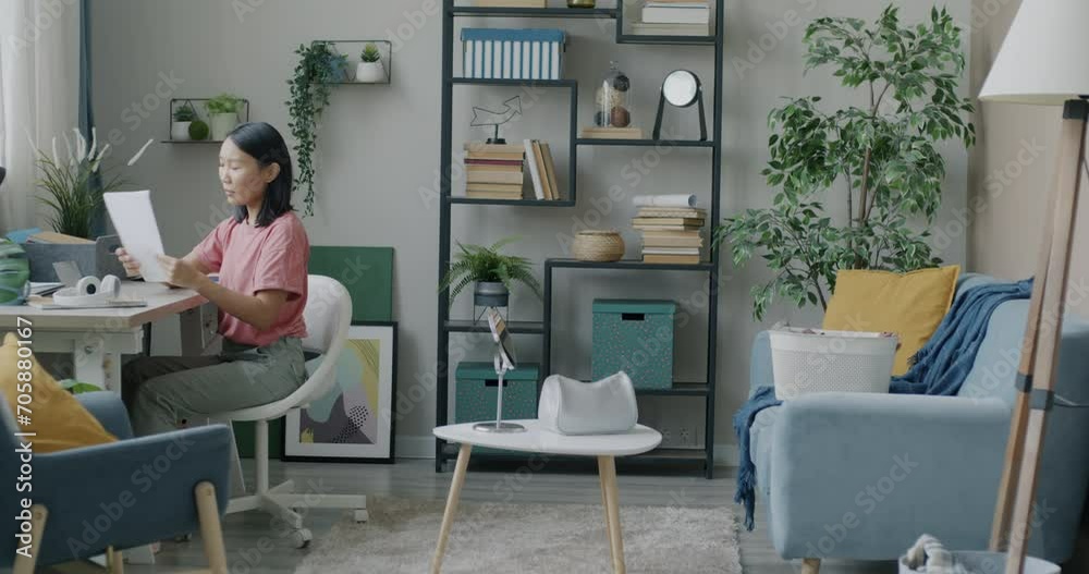 Carefree young Asian lady cleaning table sorting papers doing housework in tidy apartment. Modern people and housekeeping concept. Carefree young Asian lady cleaning table sorting papers doing housework in tidy apartment. Modern people and housekeeping concept.