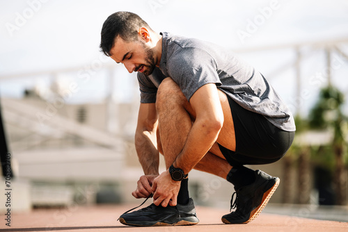 Sports man tying shoe laces in preparation for running training. Handsome young male getting ready to workout.