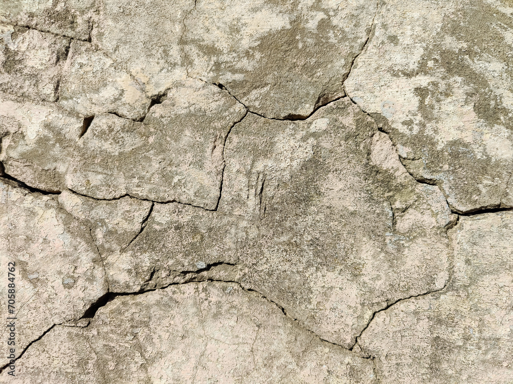 Obraz premium The stone wall of an old building with crumbling plaster and many winding, deep cracks. Copy space. Selective focus.