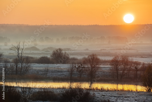 Beautiful landscape of the rising Sun over a river valley with trees and meadows on a foggy morning. Nature forest-steppe late autumn or early winter with frost or snow on the grass
