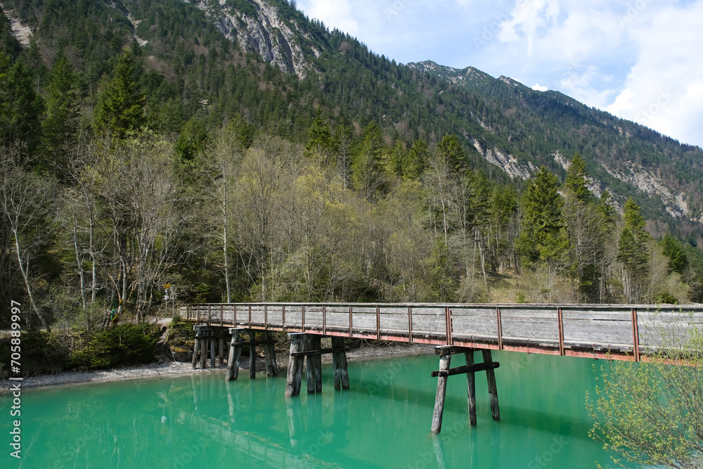 Wooden bridge on an emerald lake among trees and mountains