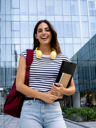 Portrait of a smiling Caucasian teenage student girl with a backpack and folder looking at camera.