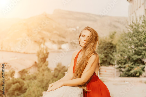 Woman red dress. Summer lifestyle of a happy woman posing near a fence with balusters over the sea.