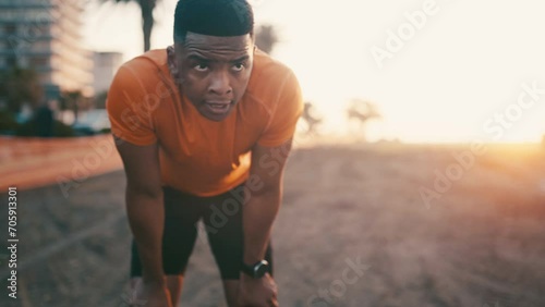 Black man, fitness and rest in sunset after exercise, outdoor cardio training or workout for recovery. Tired African male person, athlete or runner in break, breathing or sport by the city coast photo