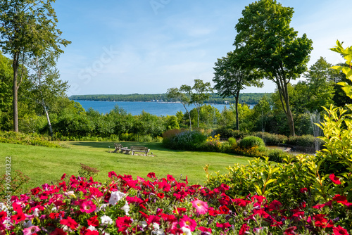 Fototapeta Naklejka Na Ścianę i Meble -  Beautiful backyard scene with colorful flowers, green grass and other vegetation, a pond with a fountain, and a lake with blue water.