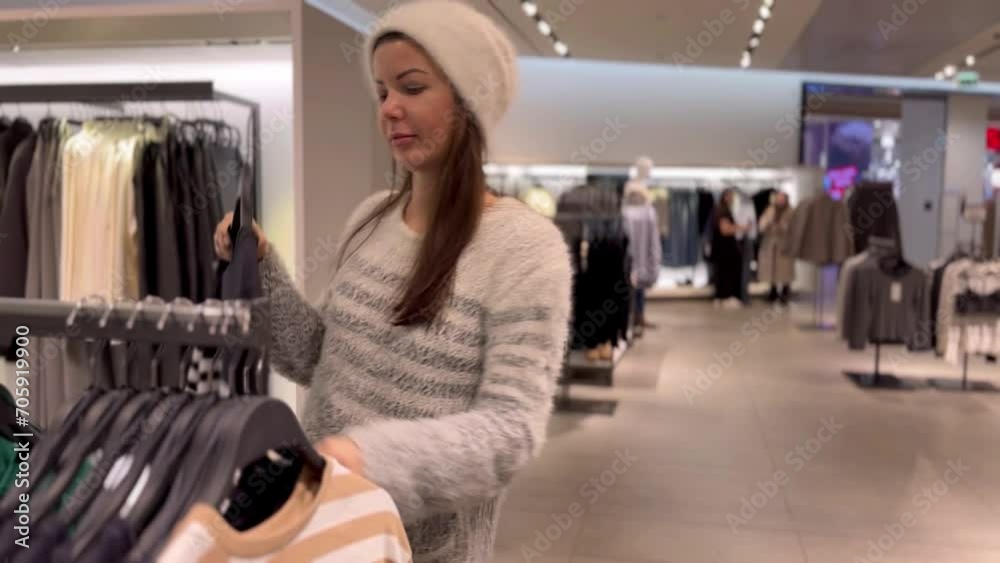 Woman chooses sweater in clothing store, puts it to herself, looking for right size. Concept of wide selection of clothes in clothing store. High quality FullHD footage Woman chooses sweater in clothing store, puts it to herself, looking for right size. Concept of wide selection of clothes in clothing store. High quality FullHD footage