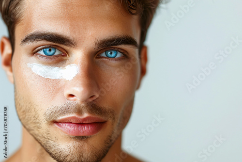 handsome young man with blue eyes has an anti-aging cream under his eye, skin care treatment photo