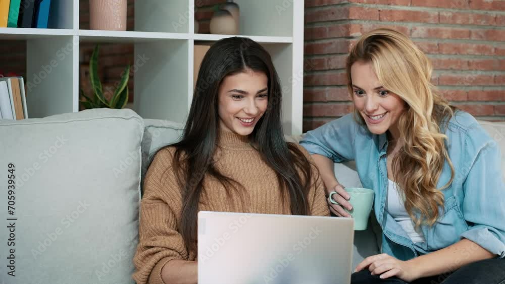 Video of two happy women friends celebrating that searching a trip together with laptop sitting on the couch at home.