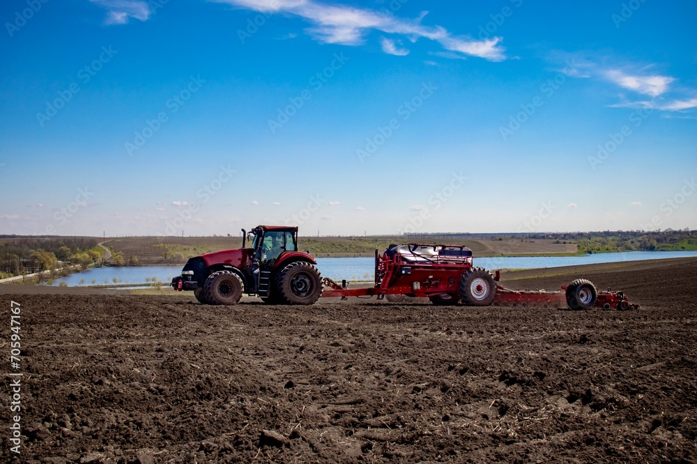 Red tractor with red planter sowing corn in a field Red tractor with red planter sowing corn in a field