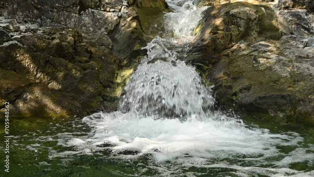 A small waterfall from a mountain stream runs into its pool (slow motion)
