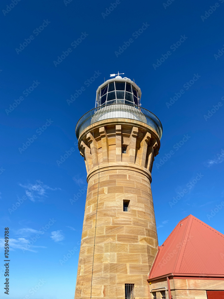 Lighthouse and red roof on the island at daytime. Sandstone lighthouse at the top of a hill. Coast ligthouse against a blue sky. Lighthouse in the harbor. Lighthouse on the coast of the region sea.