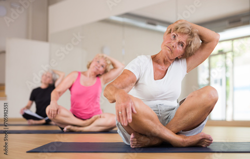 Portrait of senior woman performing stretching between asanas during group yoga training at gym. Fitness and Hatha yoga concept.