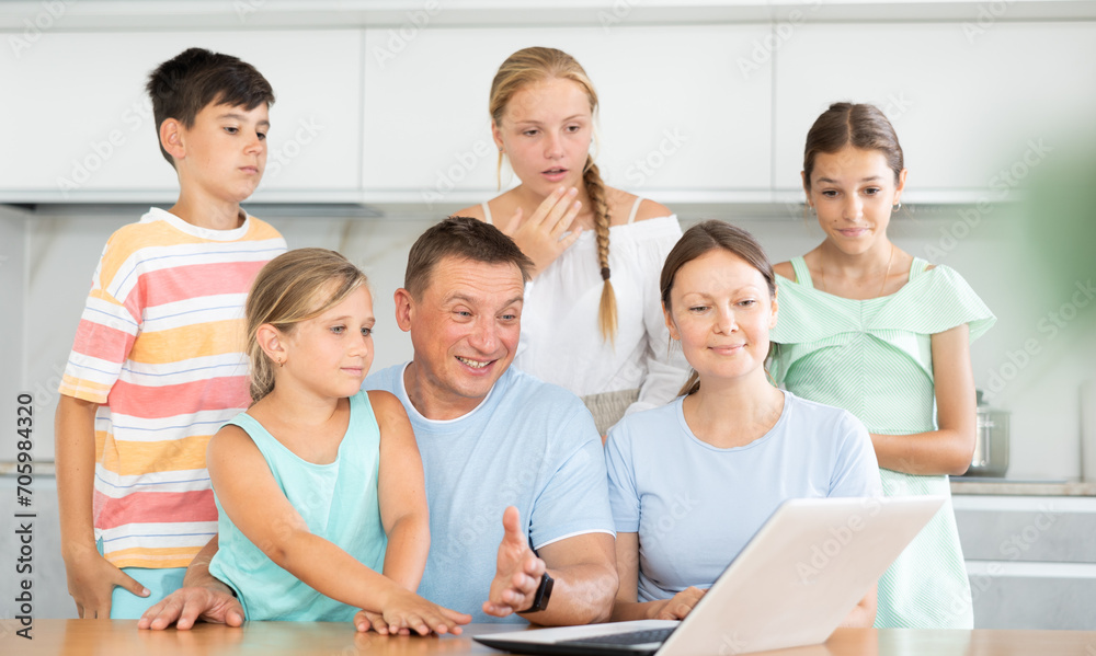 Fototapeta premium Husband, wife and children sit in front of laptop screen and communicate via video and relatives. Convenient and accessible communication with family and friends at any time of day