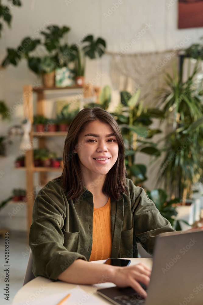 Young plant store worker posing at her workplace while working on laptop Young plant store worker posing at her workplace while working on laptop