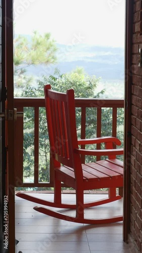 Red wooden rocking chair on balcony, swinging without anybody sitting on them.  photo