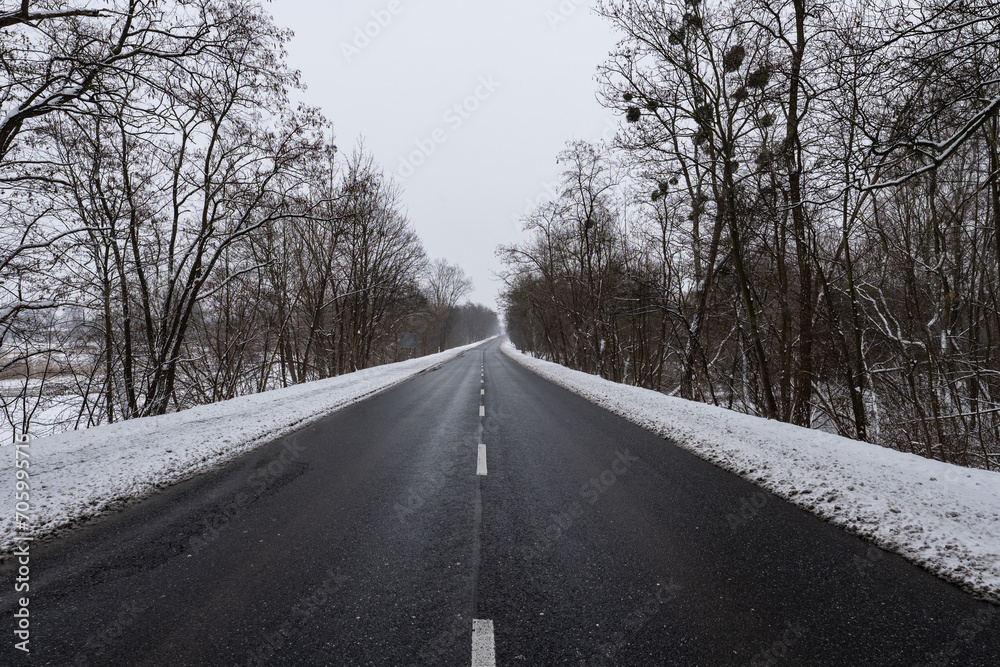 Panorama ulicy zimą, droga biegnąca wzdłuż kadru w śnieżny dzień o wieczornej porze w zachodniej Polsce