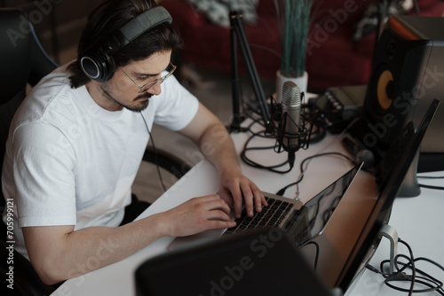 An audio producer immersed in his work, editing tracks on a laptop in a professional home studio setup