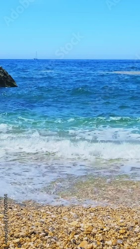 Clear blue waves beat yellow pebbles on beach on sunny summer day, Greece. Vacations, relax.  photo
