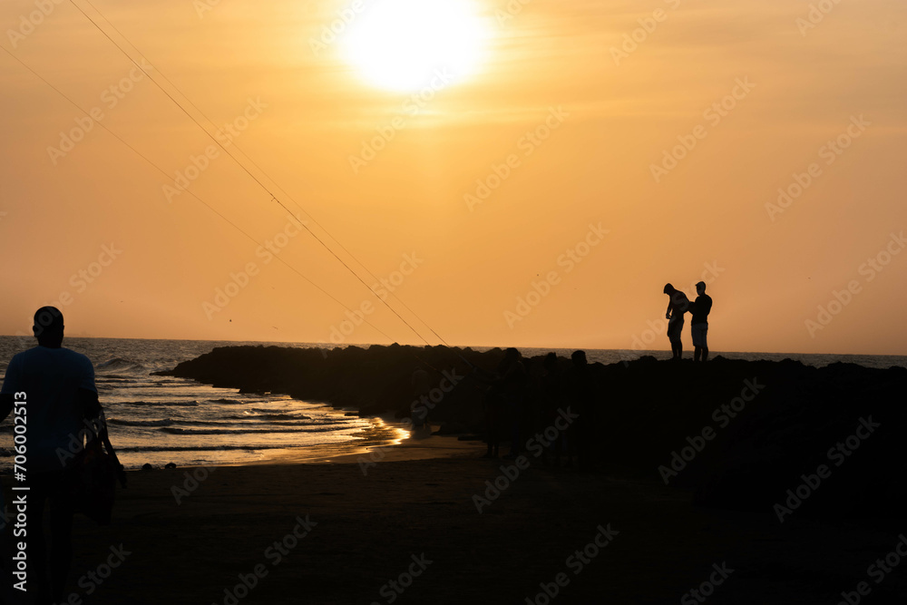 people in silhouette on the beach next to the sea with sunset. Cartagena Colombia.