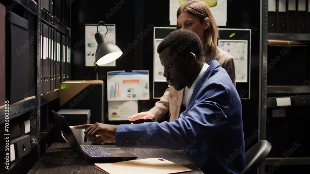 In police department, caucasian and african american law enforcement officials methodically analyze evidence and share information. Private detective and female colleague investigating criminal cases. - obrazy, fototapety, plakaty 