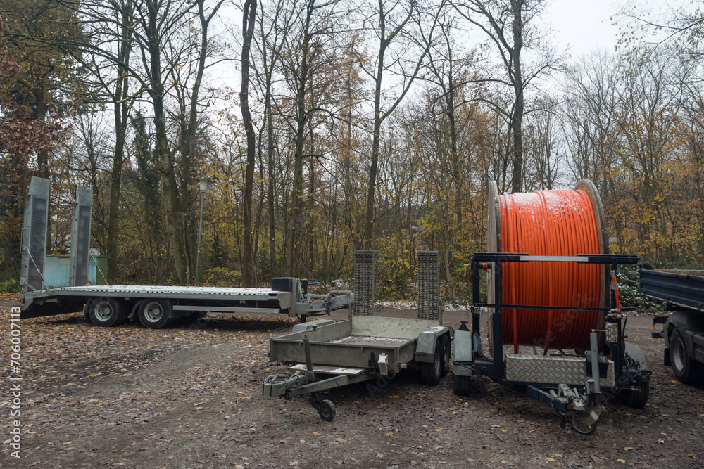 Car trailers and wooden reel with orange cable on autumn forest background. Car trailers and wooden reel with orange cable on autumn forest background.
