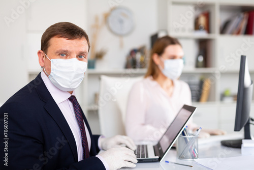 Portrait of busy entrepreneur in medical face mask and latex gloves working with female coworker in office. Concept of precautions and social distancing in coronavirus pandemic..