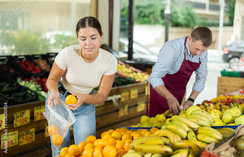 Girl buyer collects selects products in store according to list for weekly purchase. Young female customer made beeline for fresh produce section, pick juiciest oranges for morning smoothies
