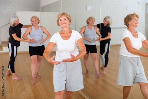 Elderly women who are engaged in the dance section at a group lesson stand in the 1st position of the ballet stand, where ..the choreographer helps them to do it correctly photo