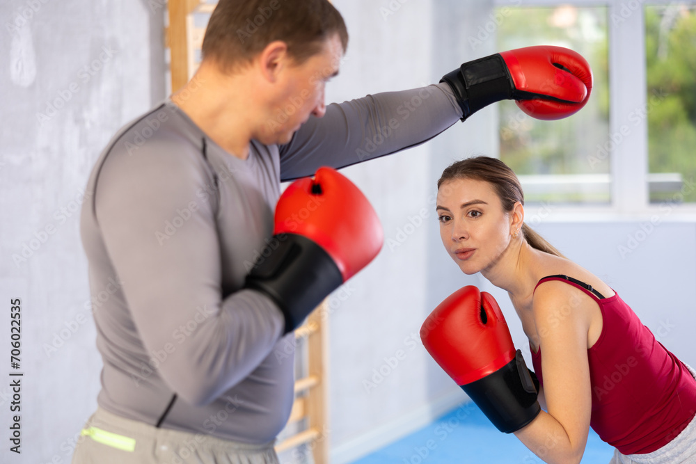 Adult man and young woman in boxing gloves boxing in gym