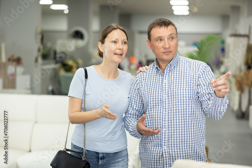 Spouses scan make inspection furniture store, searching for perfect item to complete living space. Buyers looks around in showroom, determined to find ideal piece to elevate aesthetic of living area