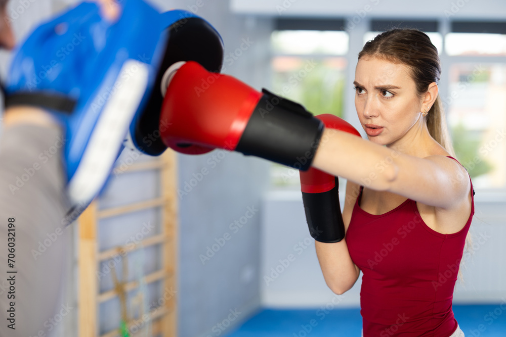 Adult man in punch mitts and young woman training boxing punches in studio