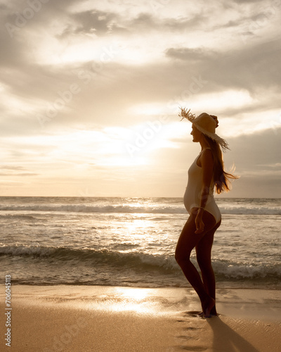 Happy pregnant woman with on beach look at sunset . Cheerful expectant mother standing on beach. Pregnancy concept
