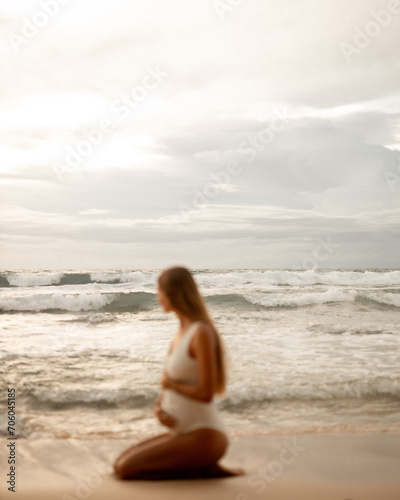 Blurred image unfocused pregnant woman sit on the beach, focus at the ocean waves © Yevhenii