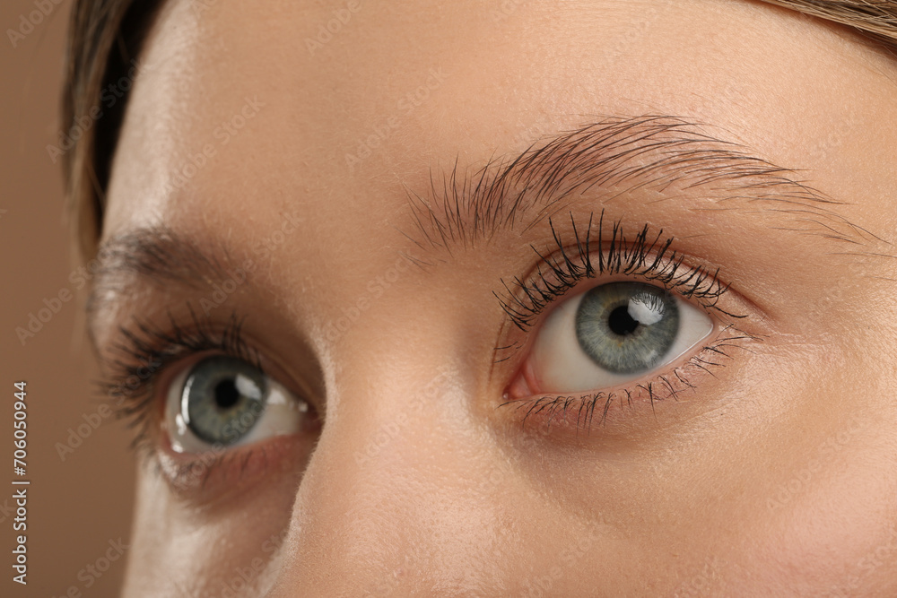 Naklejka premium Woman with long eyelashes after mascara applying against light brown background, closeup