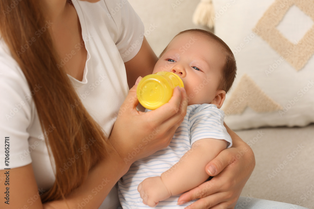 Mother feeding her cute child with infant formula indoors