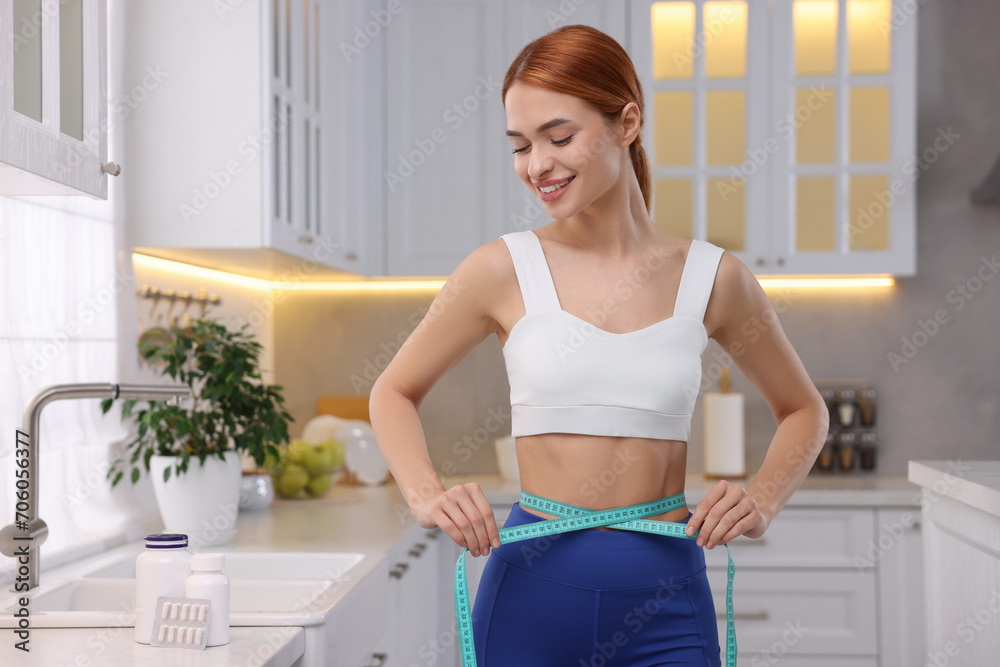 Slim woman measuring waist with tape in kitchen. Weight loss Slim woman measuring waist with tape in kitchen. Weight loss
