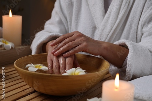 Woman soaking her hands in bowl of water and flowers at wooden table, closeup. Spa treatment photo