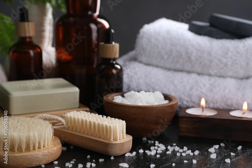 Spa composition. Brushes, soap bar, sea salt and burning candles on black table, closeup