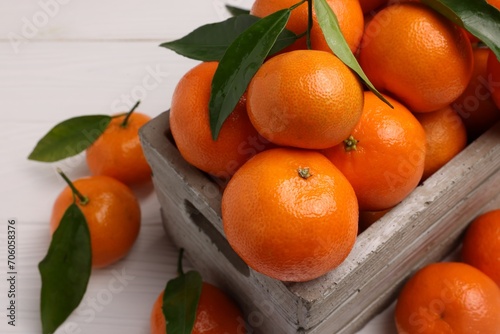 Delicious tangerines with leaves in crate on white wooden table, closeup