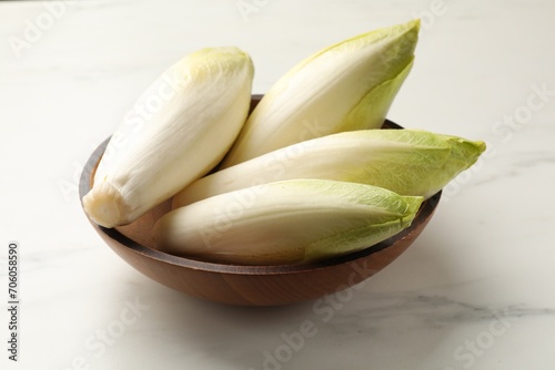 Raw ripe chicories in bowl on white marble table, closeup