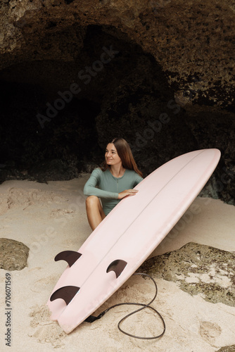 Photography A girl surfer sits near  surfboard on the beach look at the waves