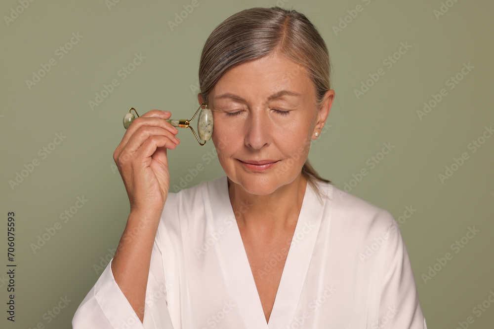 Woman massaging her face with jade roller on green background Woman massaging her face with jade roller on green background