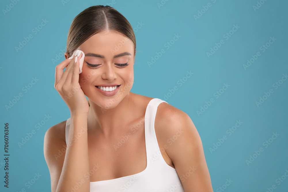 Beautiful woman removing makeup with cotton pad on light blue background. Space for text Beautiful woman removing makeup with cotton pad on light blue background. Space for text