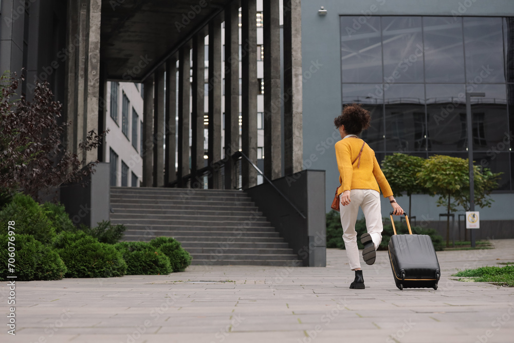 Being late. Woman with suitcase running towards building outdoors, back view