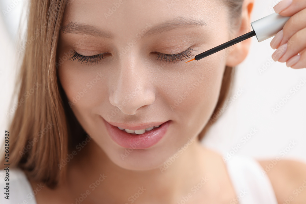 Beautiful woman applying serum onto eyelashes indoors, closeup