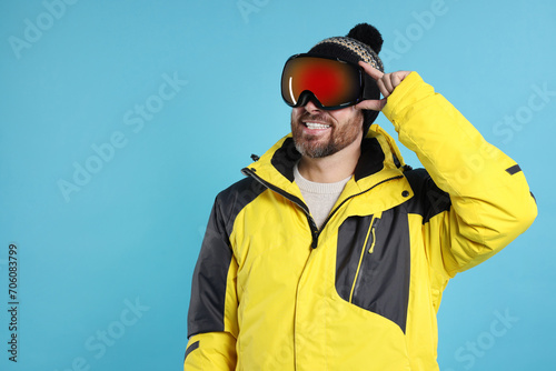Winter sports. Happy man in ski suit and goggles on light blue background, space for text © New Africa